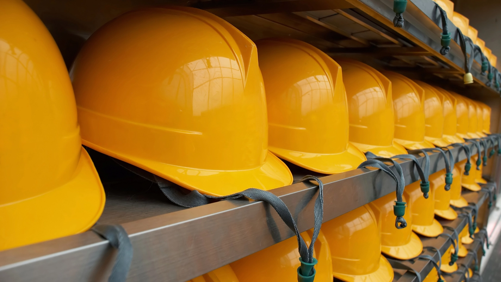 Viele gelbe Schutzhelme liegen in mehreren Reihen neben- und übereinander in einem Regal als Symbol für Arbeitssicherheit.